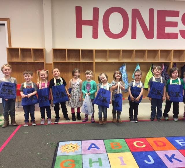 Group of children wearing blue aprons standing in a classroom