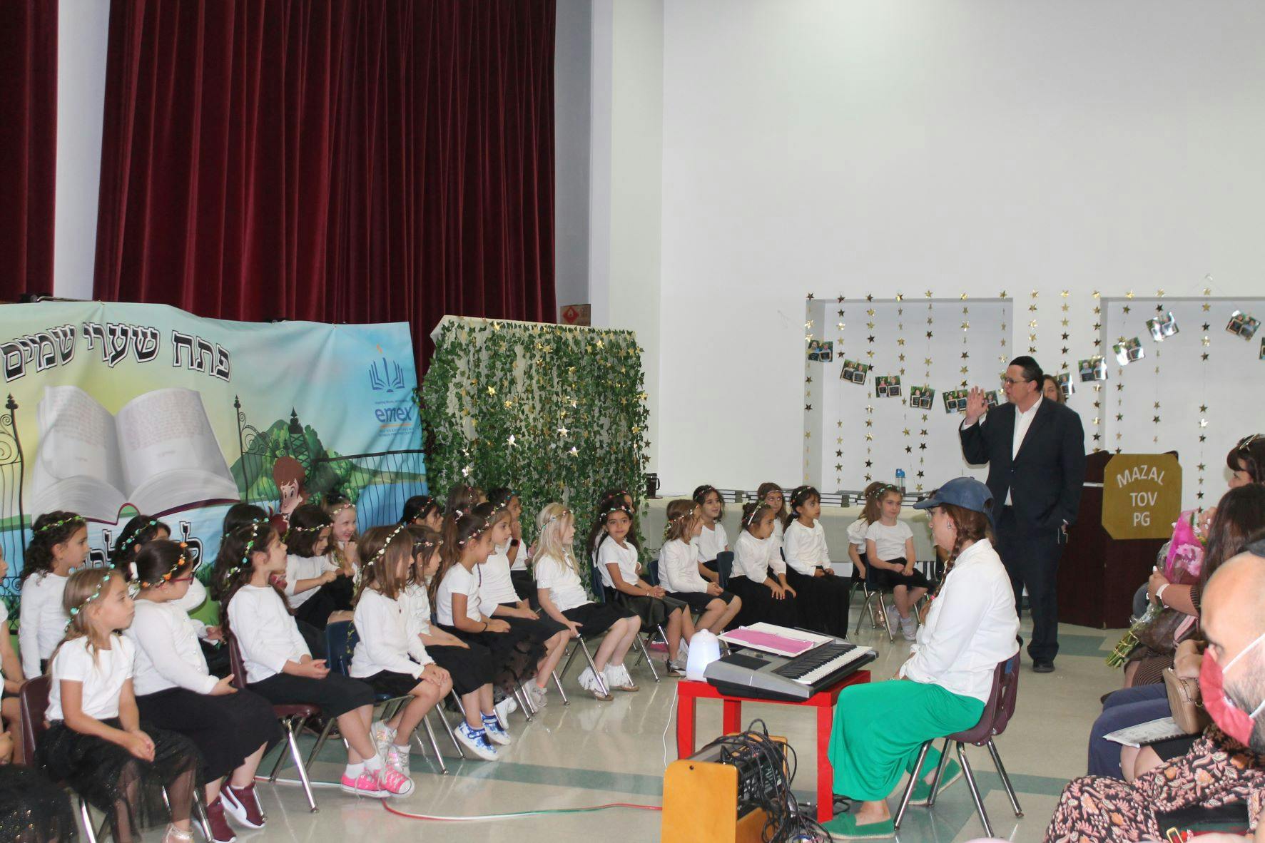 Adults and children on stage in an auditorium with Mazal Tov sign