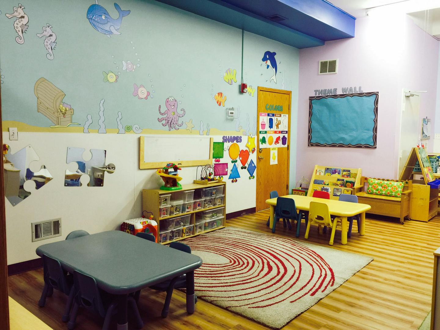 A colorful classroom with small tables and chairs, a rug, and wall decorations