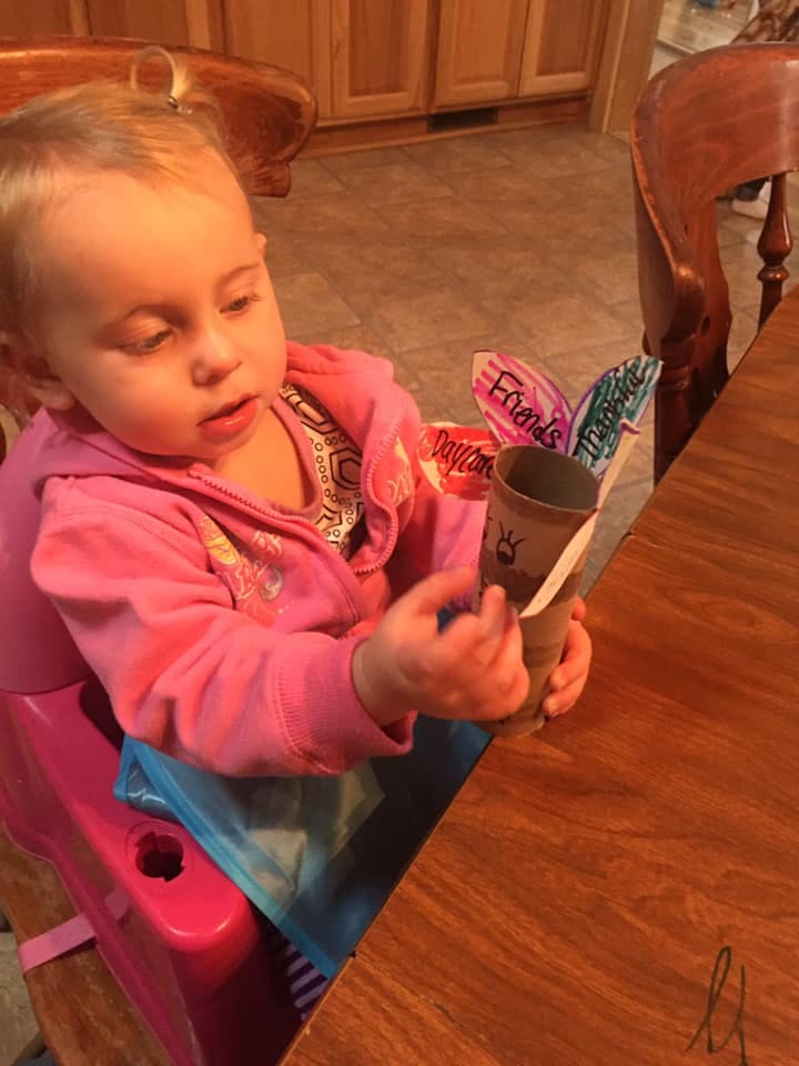 Child in a high chair holding a paper tube craft