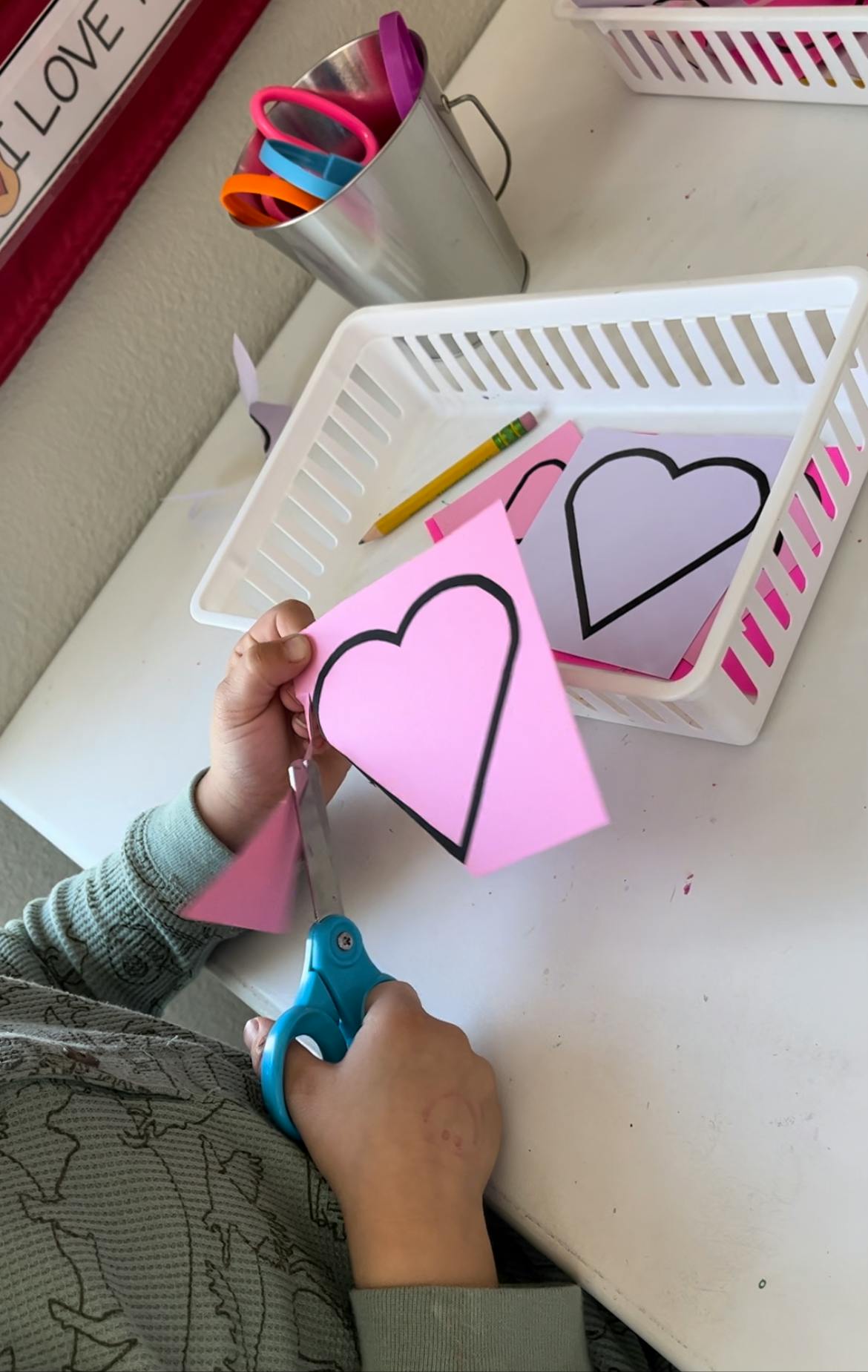 Child cutting out a pink paper heart with blue scissors