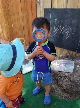 Child holding a magnifying glass to their face