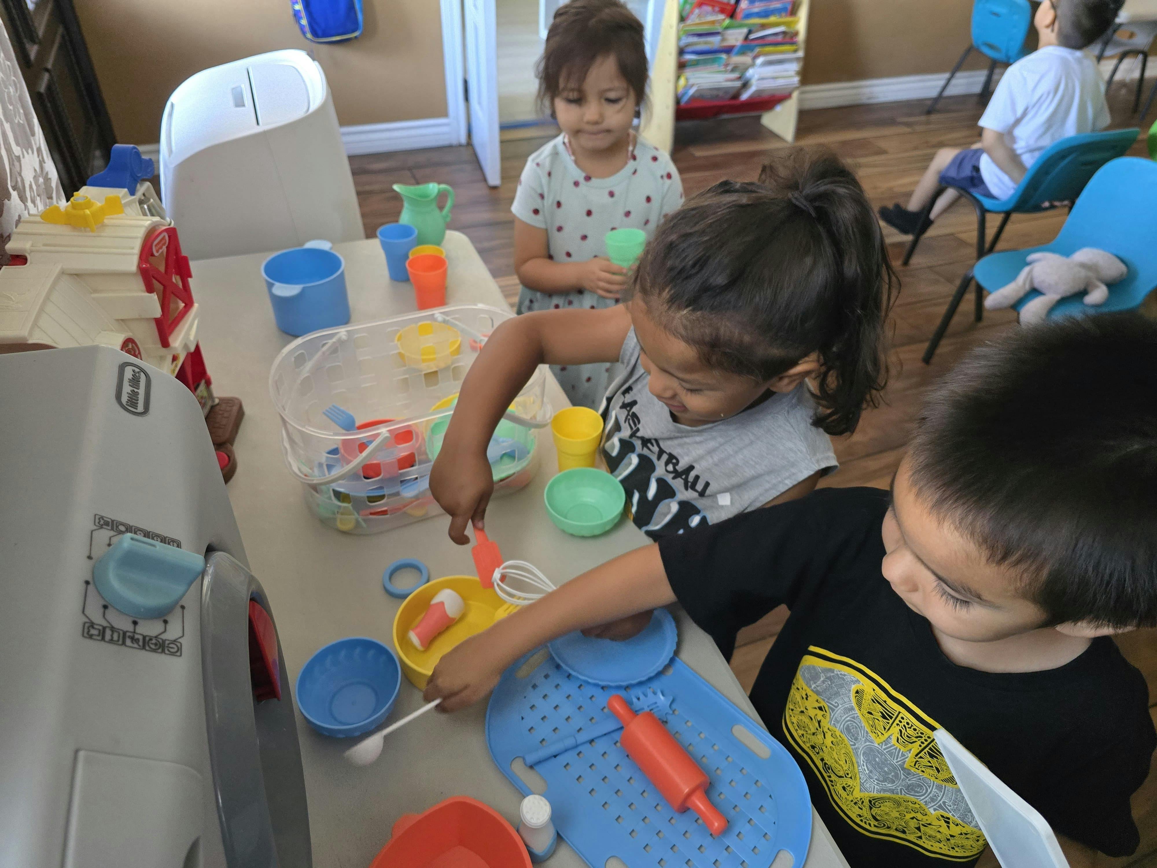 Three children playing with toy kitchen accessories at a table