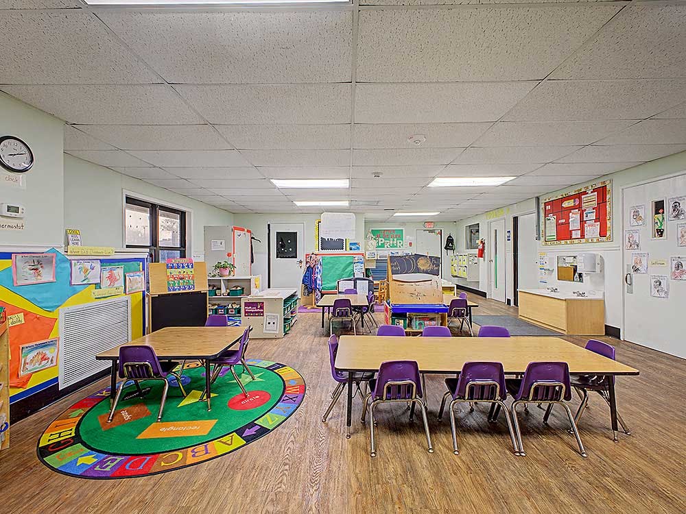 Empty classroom with tables, purple chairs, and an alphabet rug