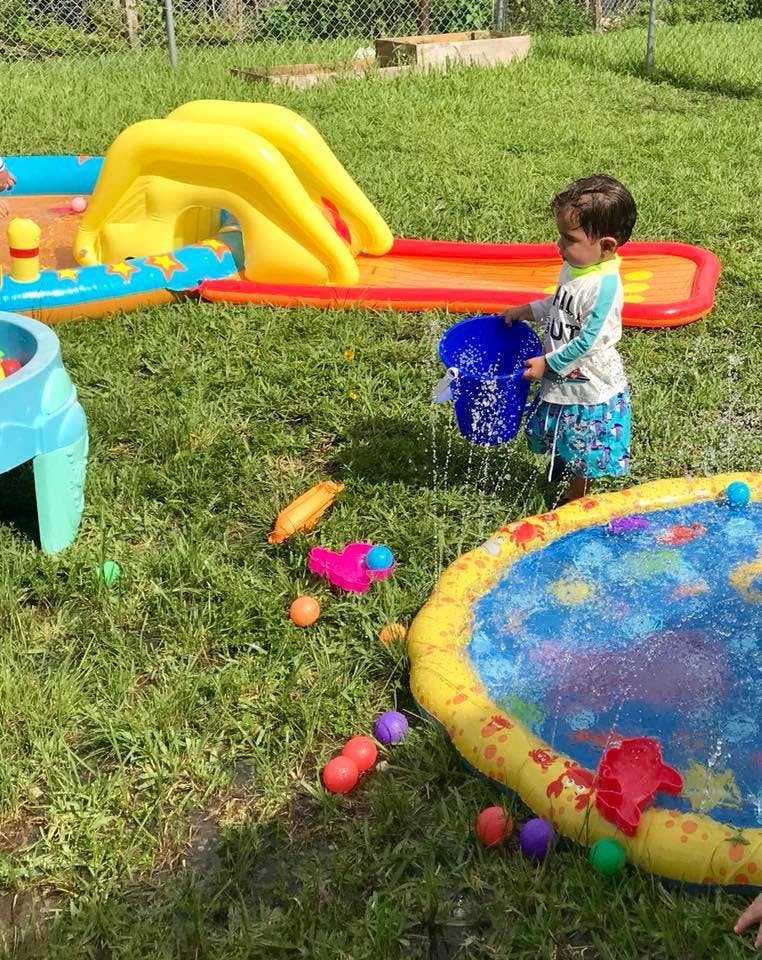 Child playing with a blue bucket and water in a grassy area