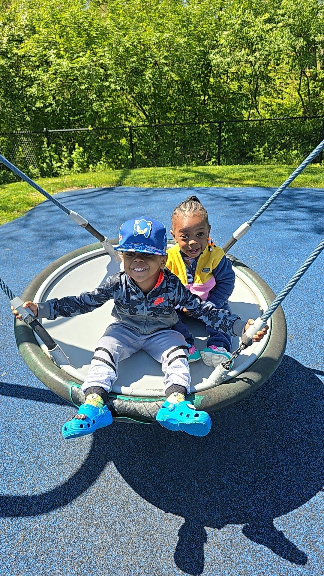 Two children sitting on a swing at a playground