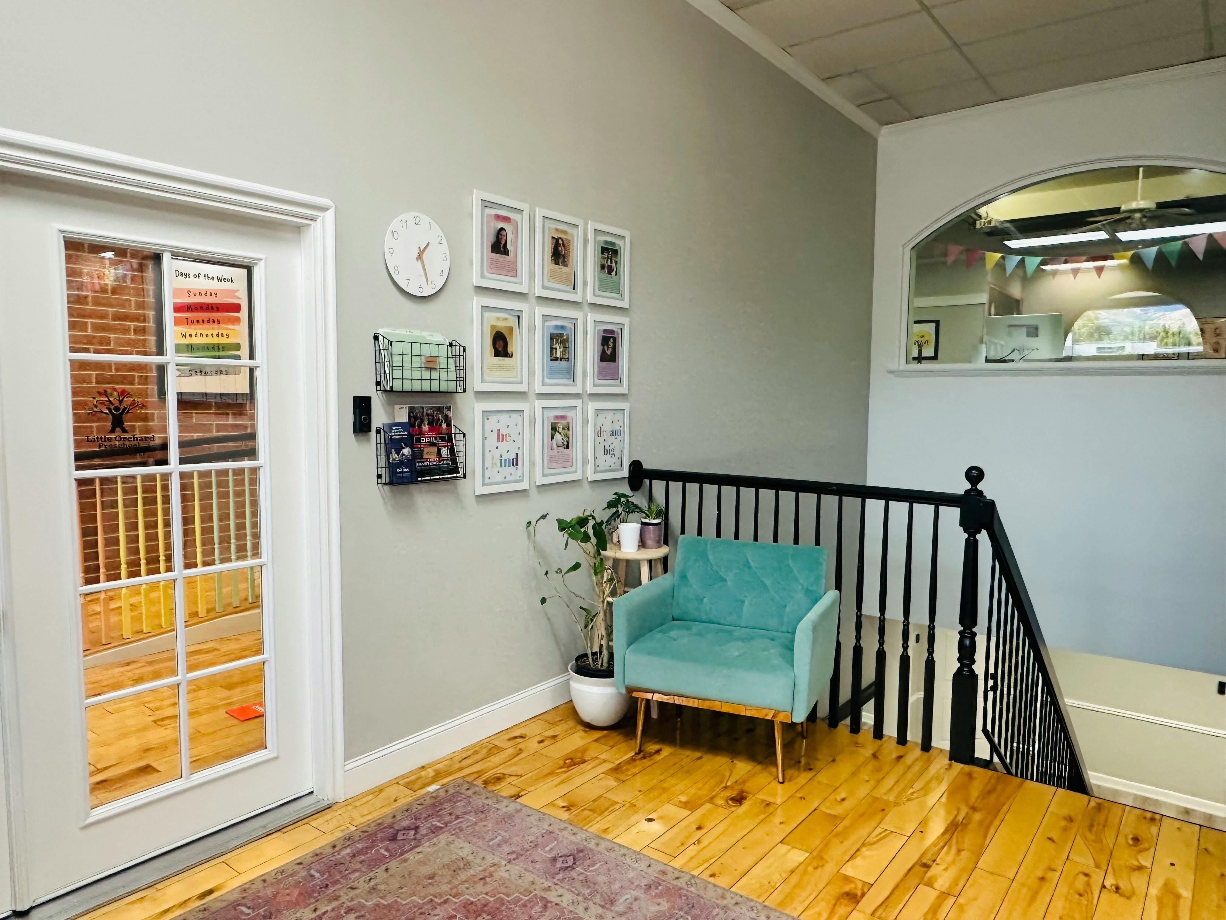 Waiting area with a teal armchair, framed pictures on the wall, and a staircase