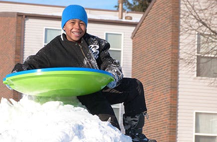 Child in winter clothing sitting on a sled in snow
