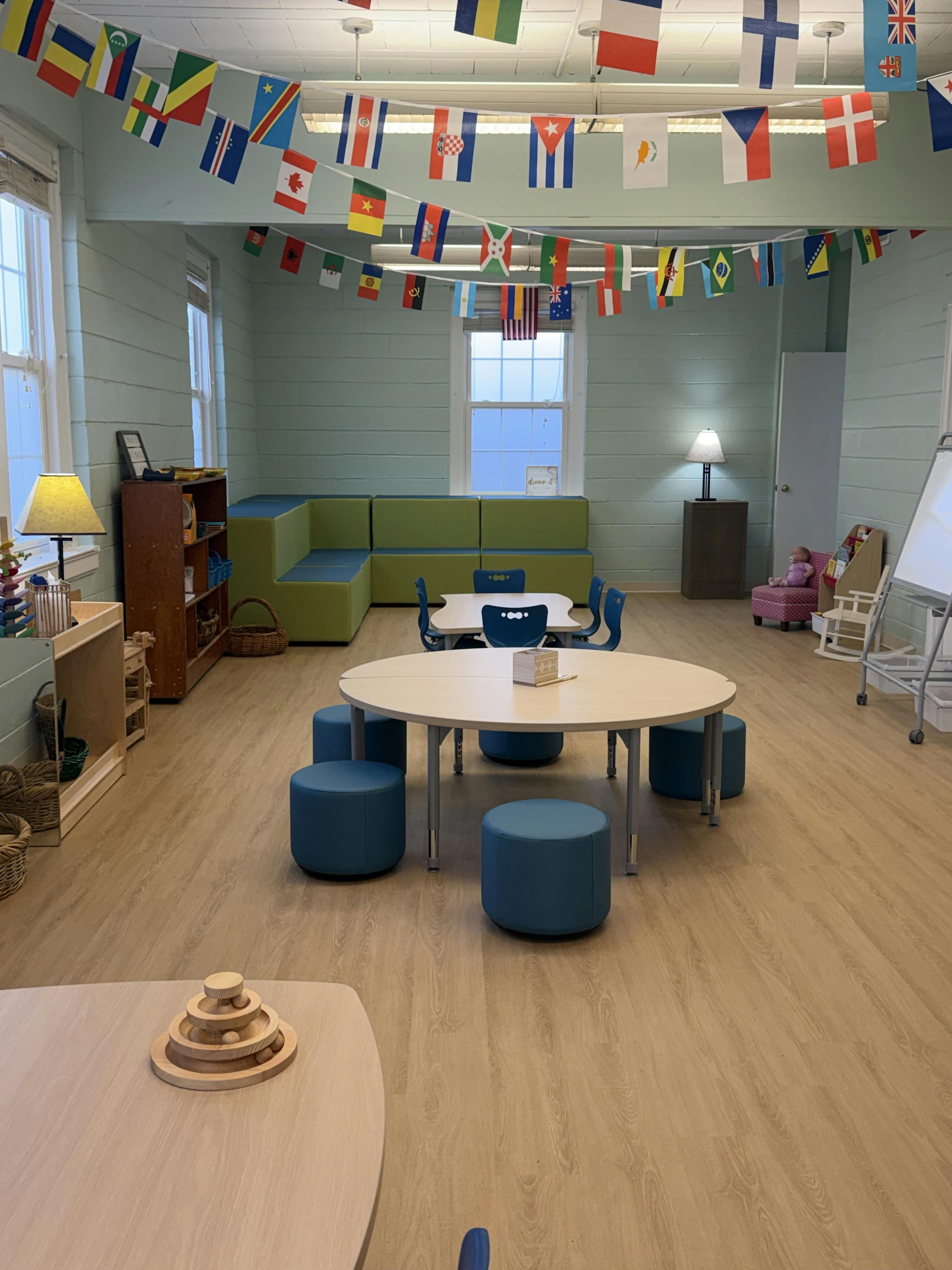 Classroom with small round tables, blue stools, and hanging international flags