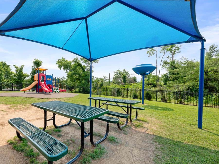 Picnic tables and benches under a blue canopy with a playground in the background