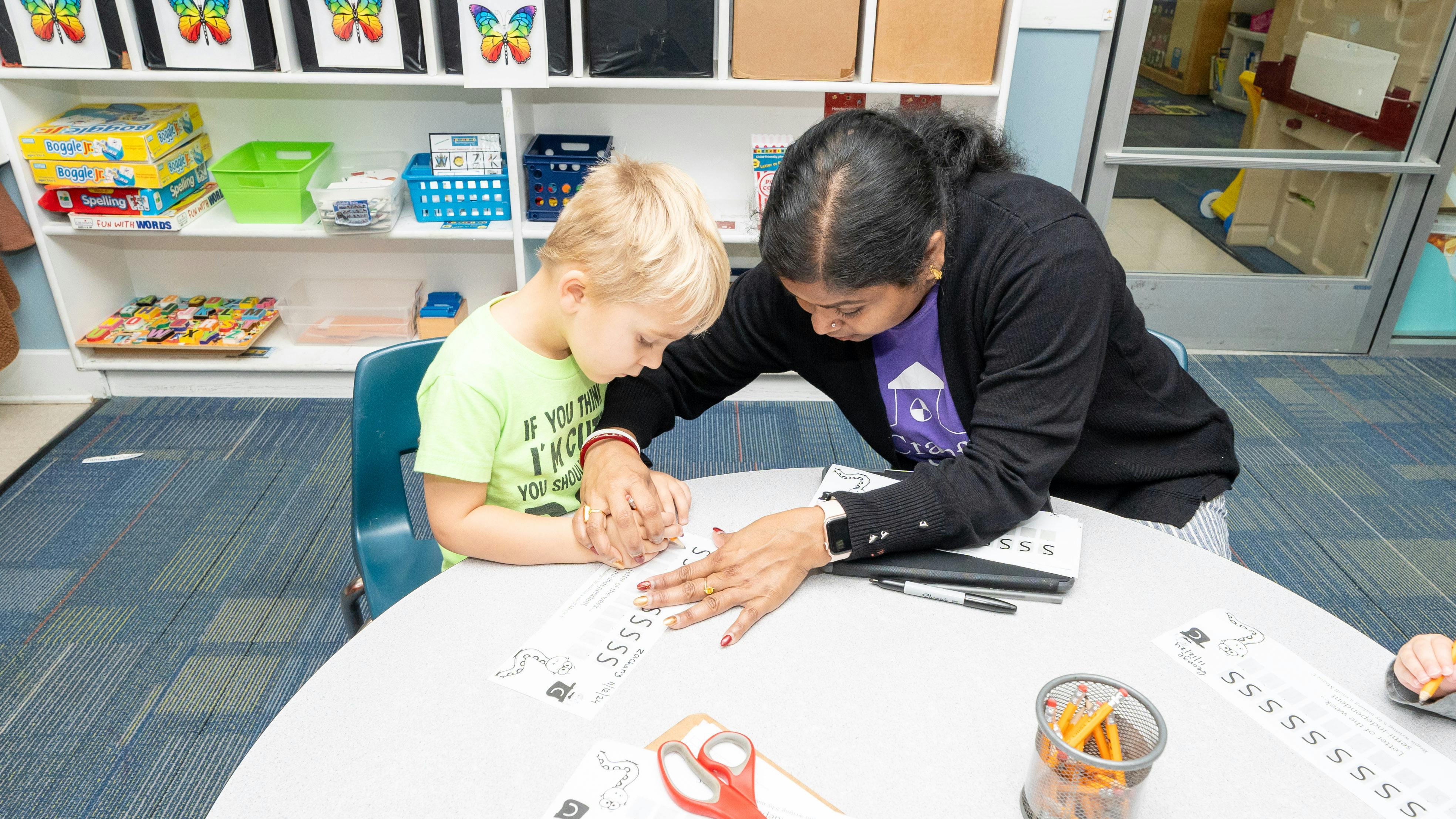 Adult and child writing at a table in a classroom