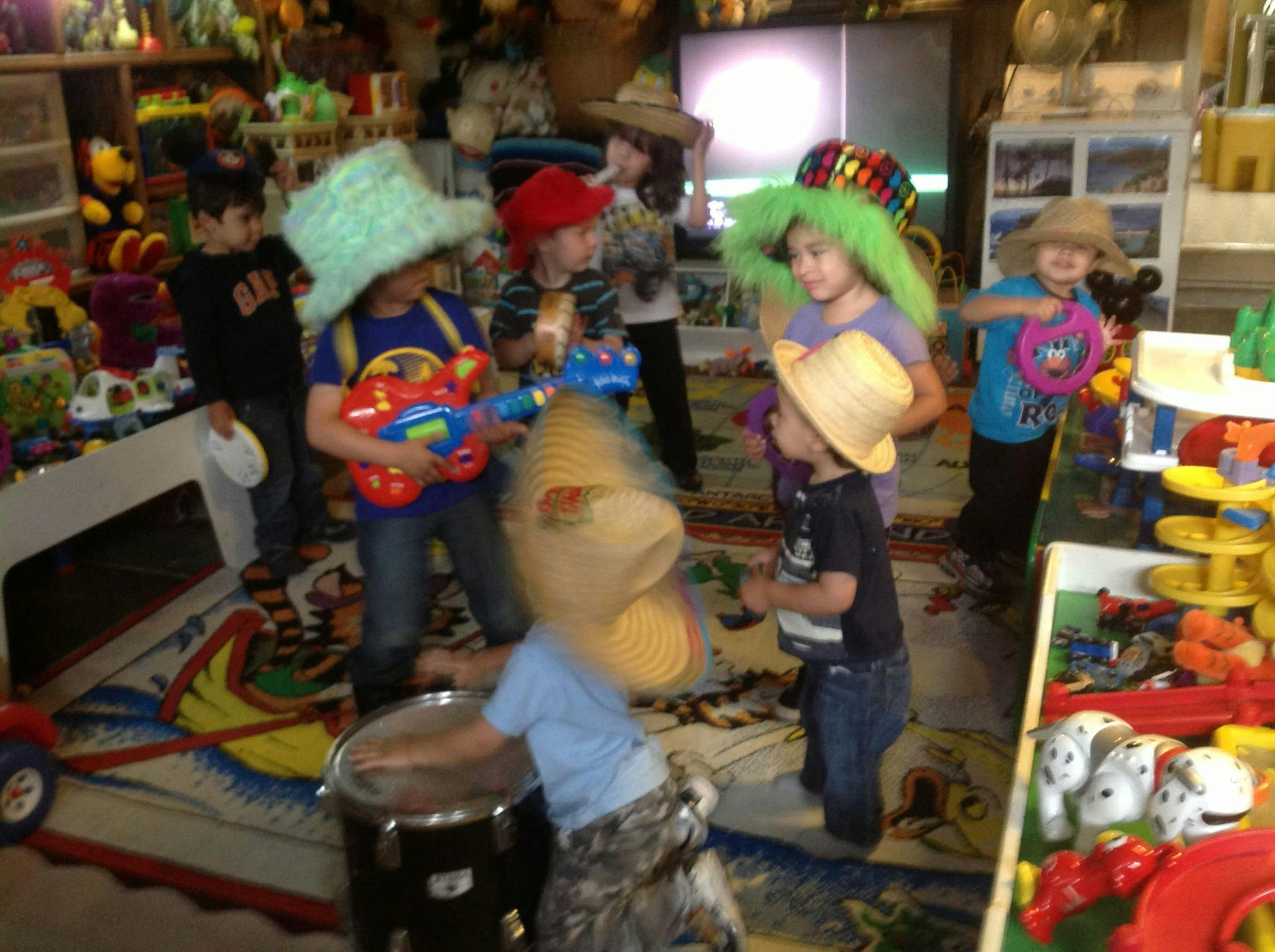 Children playing with toy instruments and wearing hats in a playroom