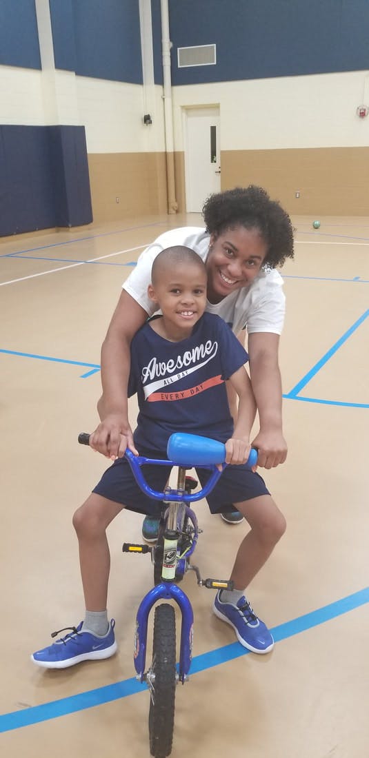 Person helping a child on a bicycle in a gym