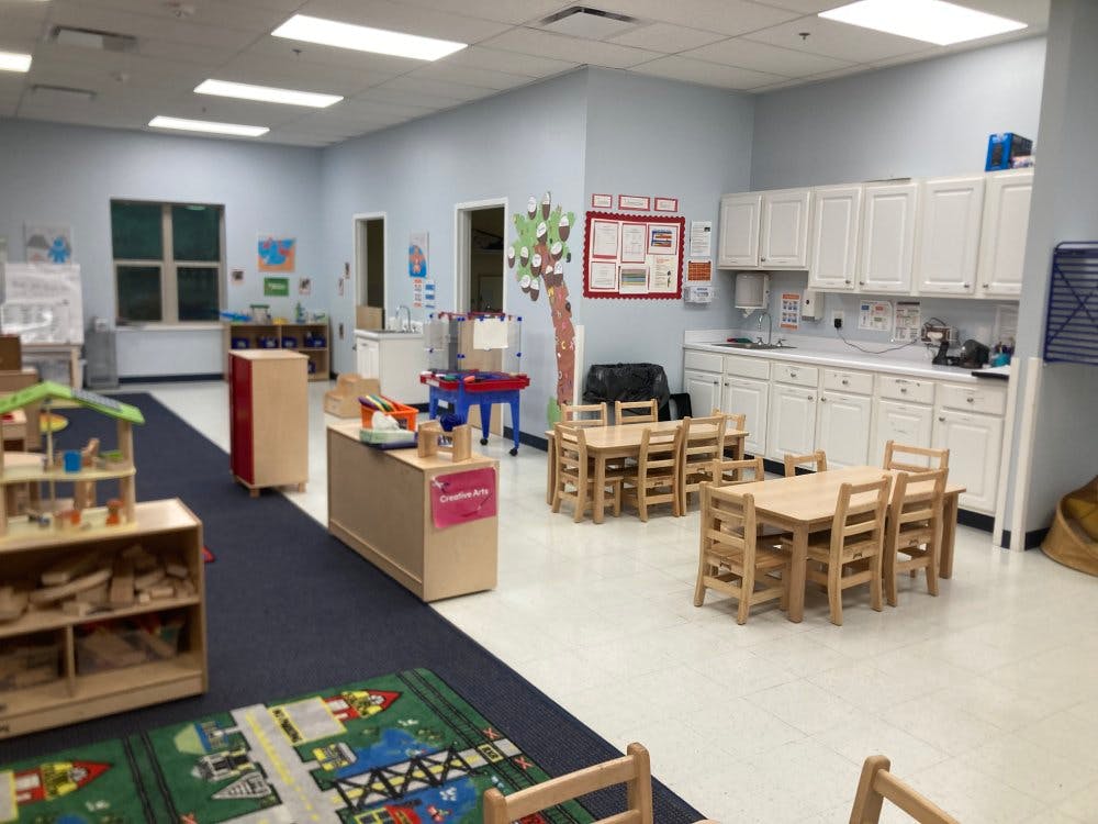 Classroom with small wooden tables and chairs, white cabinets, and play areas