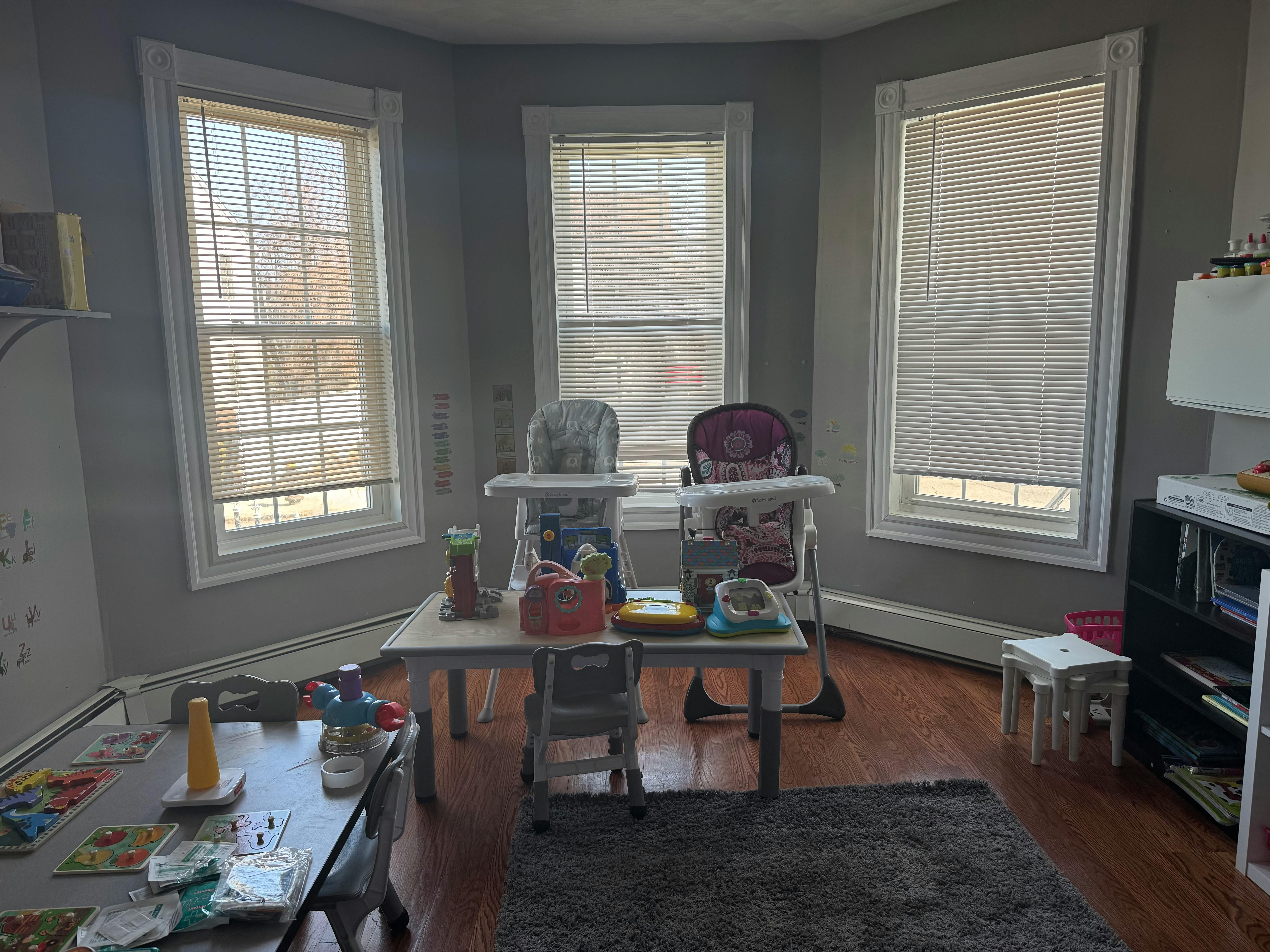 Two high chairs and a small table with toys in a room with windows