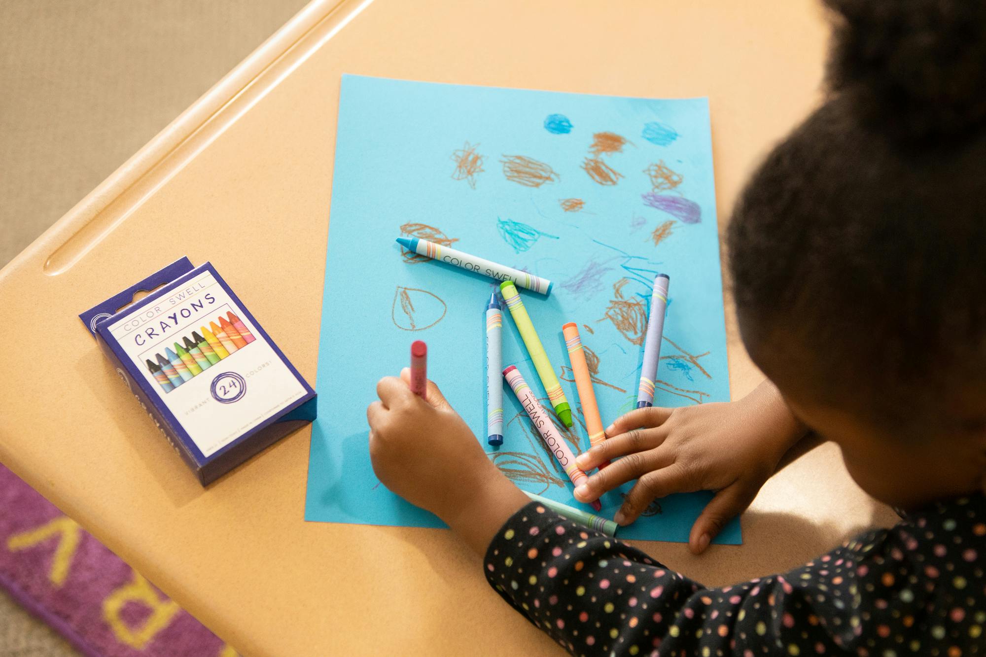 Child drawing on blue paper with crayons