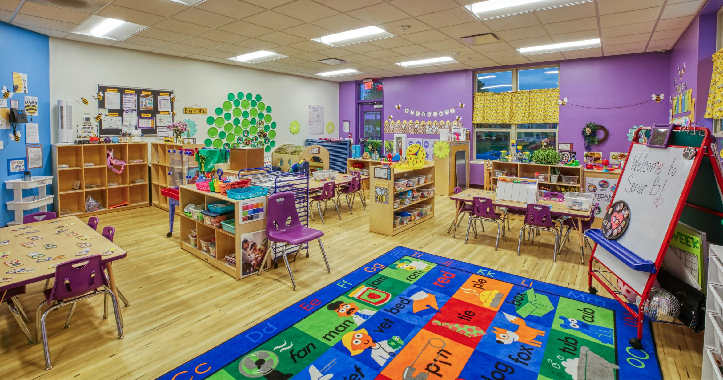 An empty early childhood classroom with colorful walls, tables, and a large alphabet rug