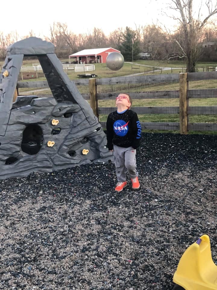 Child looking up at a ball in the air next to a climbing structure