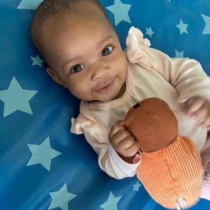 Child lying on a star-patterned mat holding a plush toy
