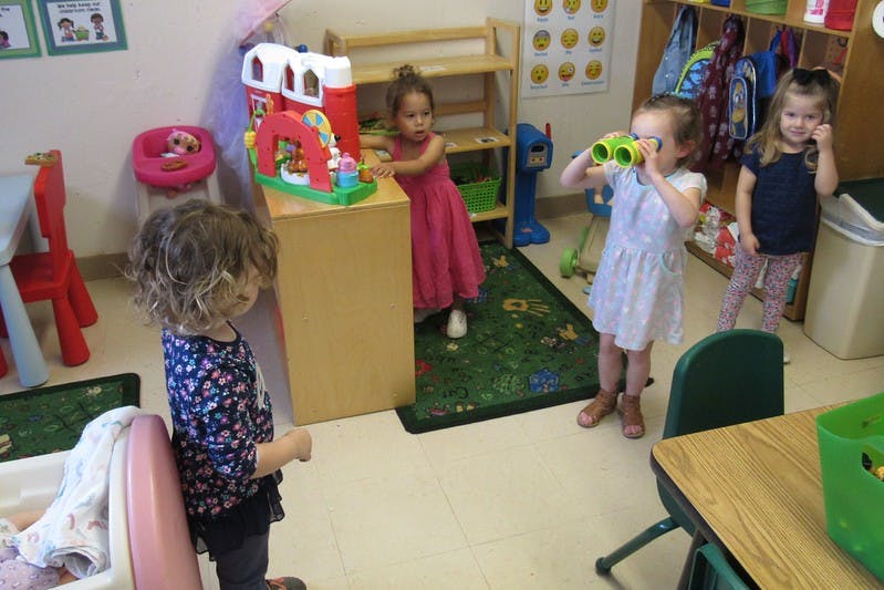 Three children playing in a classroom, one looking through binoculars