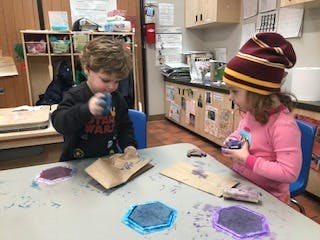 Two children doing an art activity at a table in a classroom