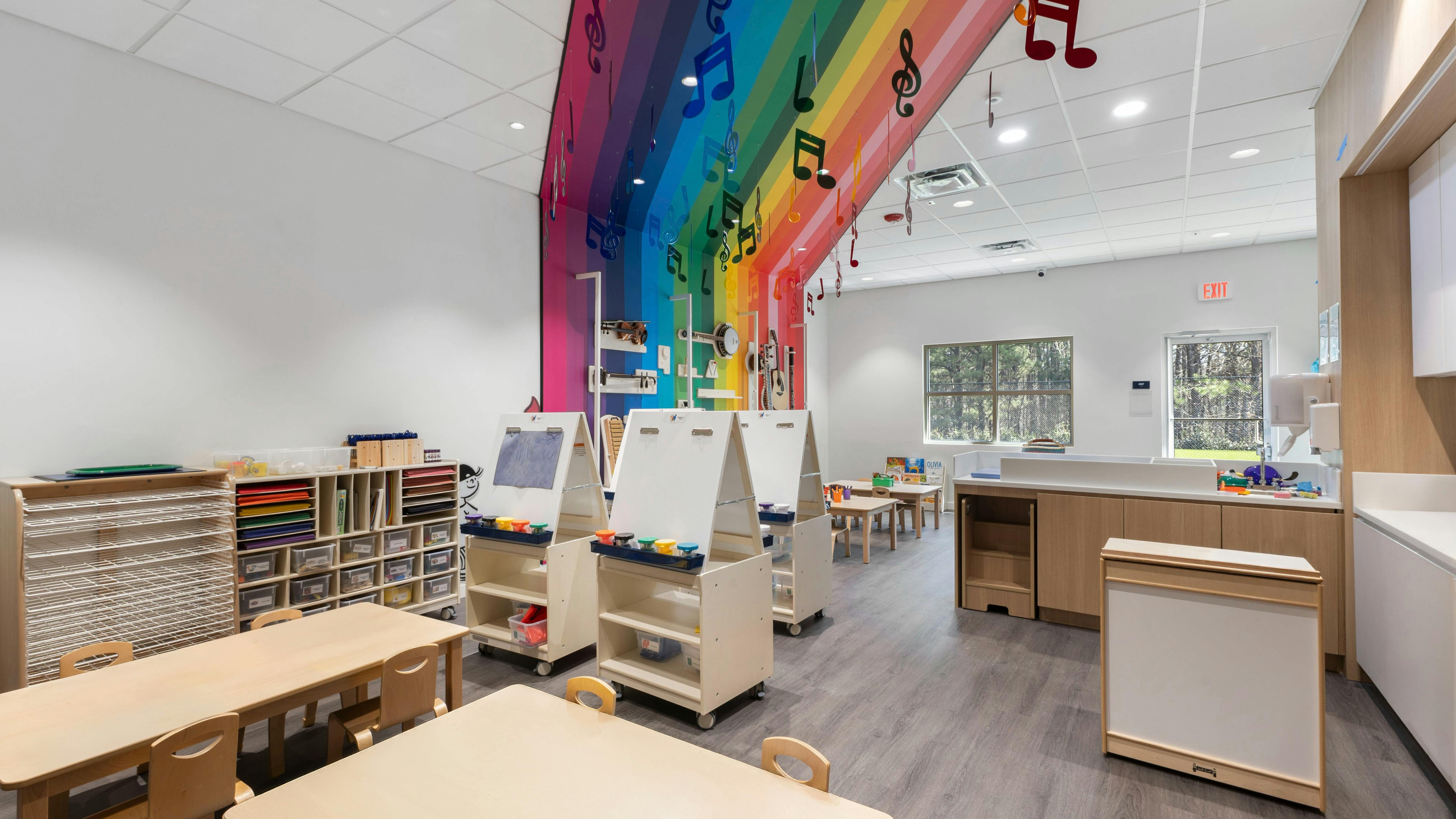 Children's classroom with small tables, easels, and a rainbow wall with musical notes