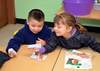 Two children looking at small packages at a table