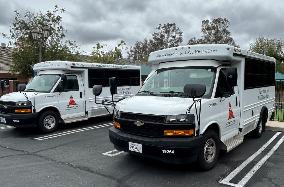 Two white KinderCare shuttle buses parked in a lot