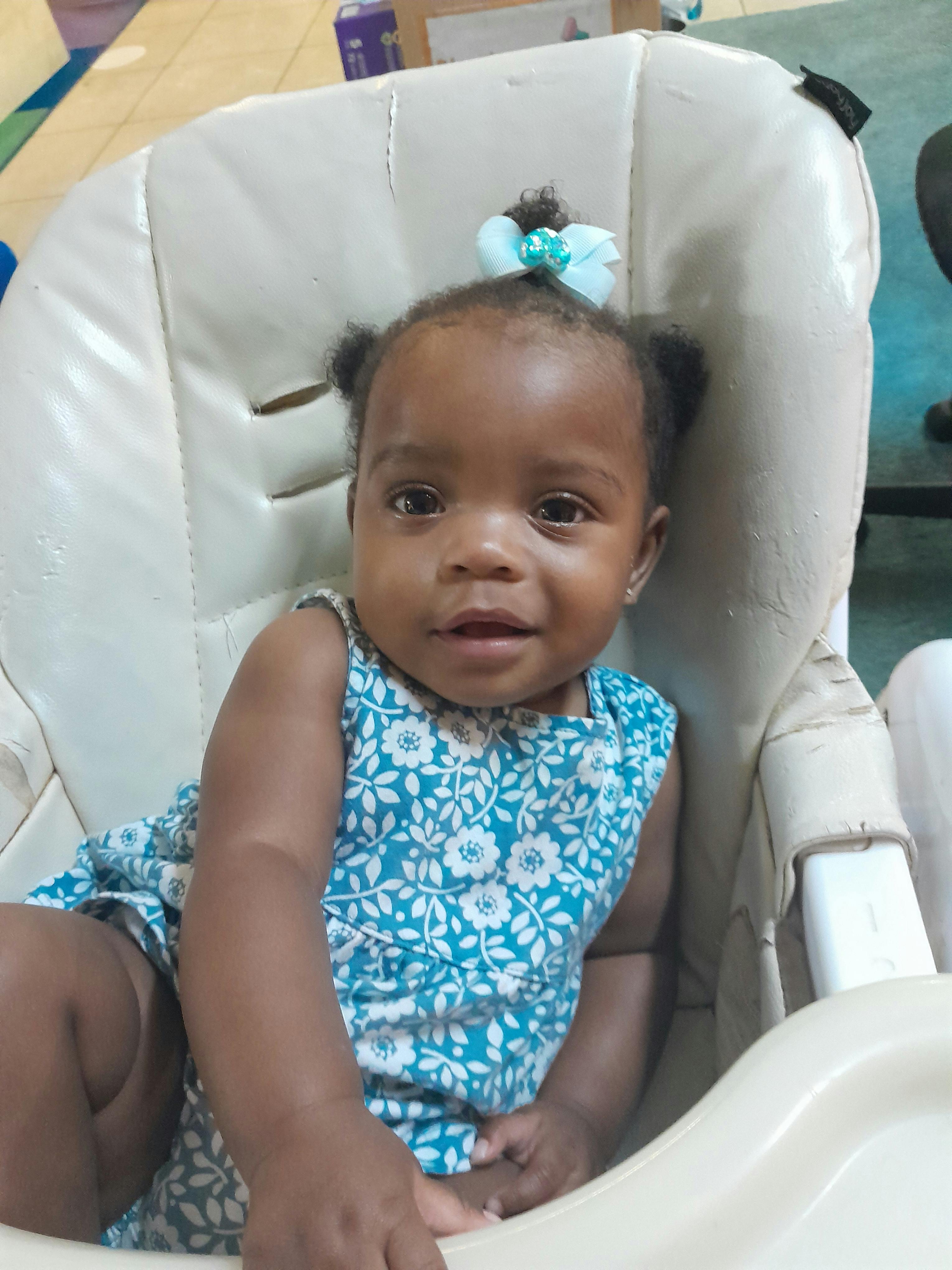 Child in a high chair wearing a blue and white floral outfit