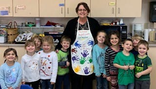 Adult wearing apron with handprints standing with children