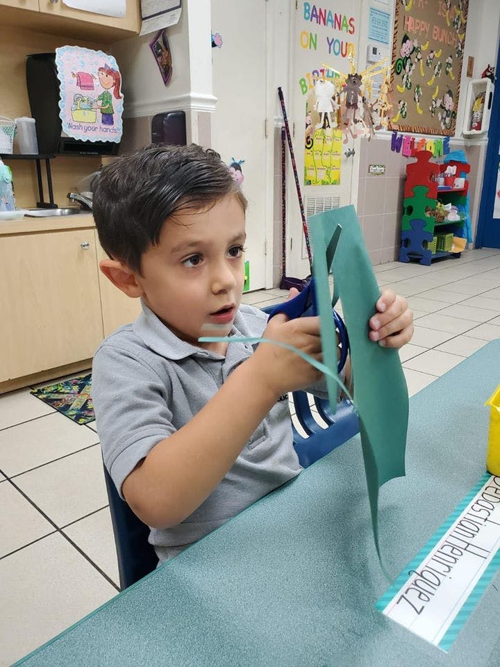 Child cutting green paper with scissors in a classroom