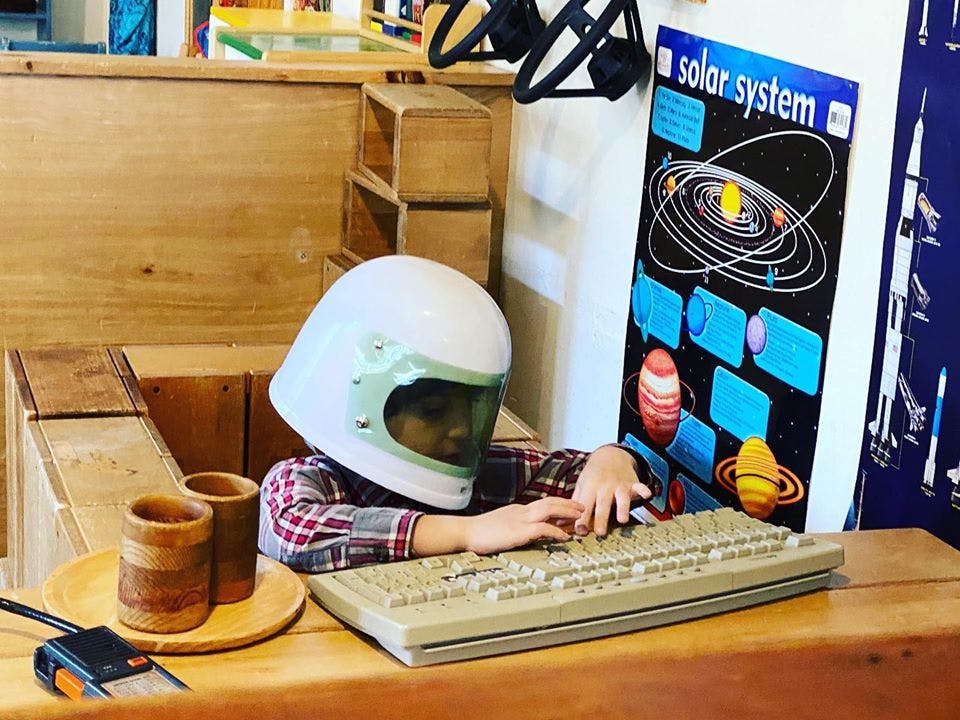 Child wearing a helmet typing on a keyboard next to a solar system poster
