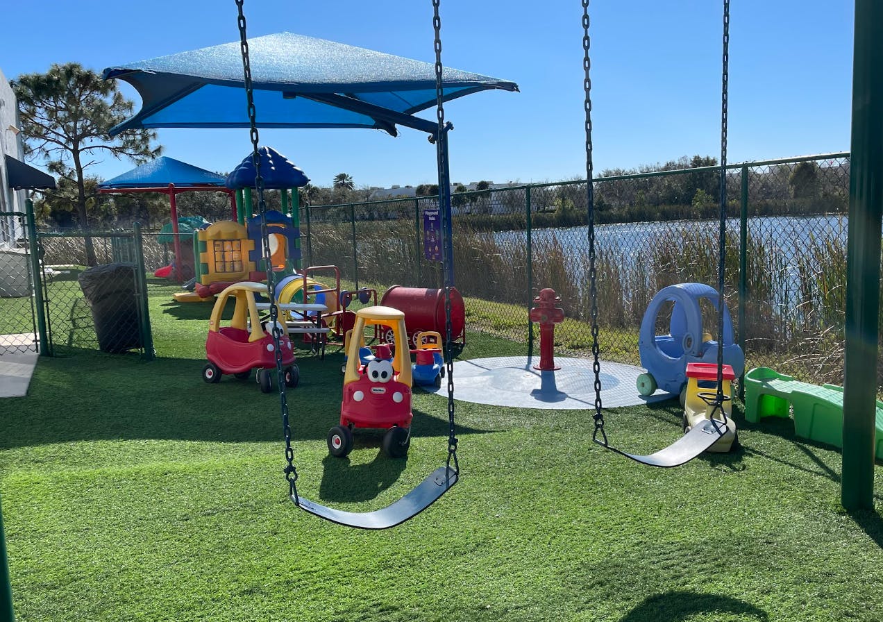 Playground with swings, ride-on cars, and a play structure next to a lake