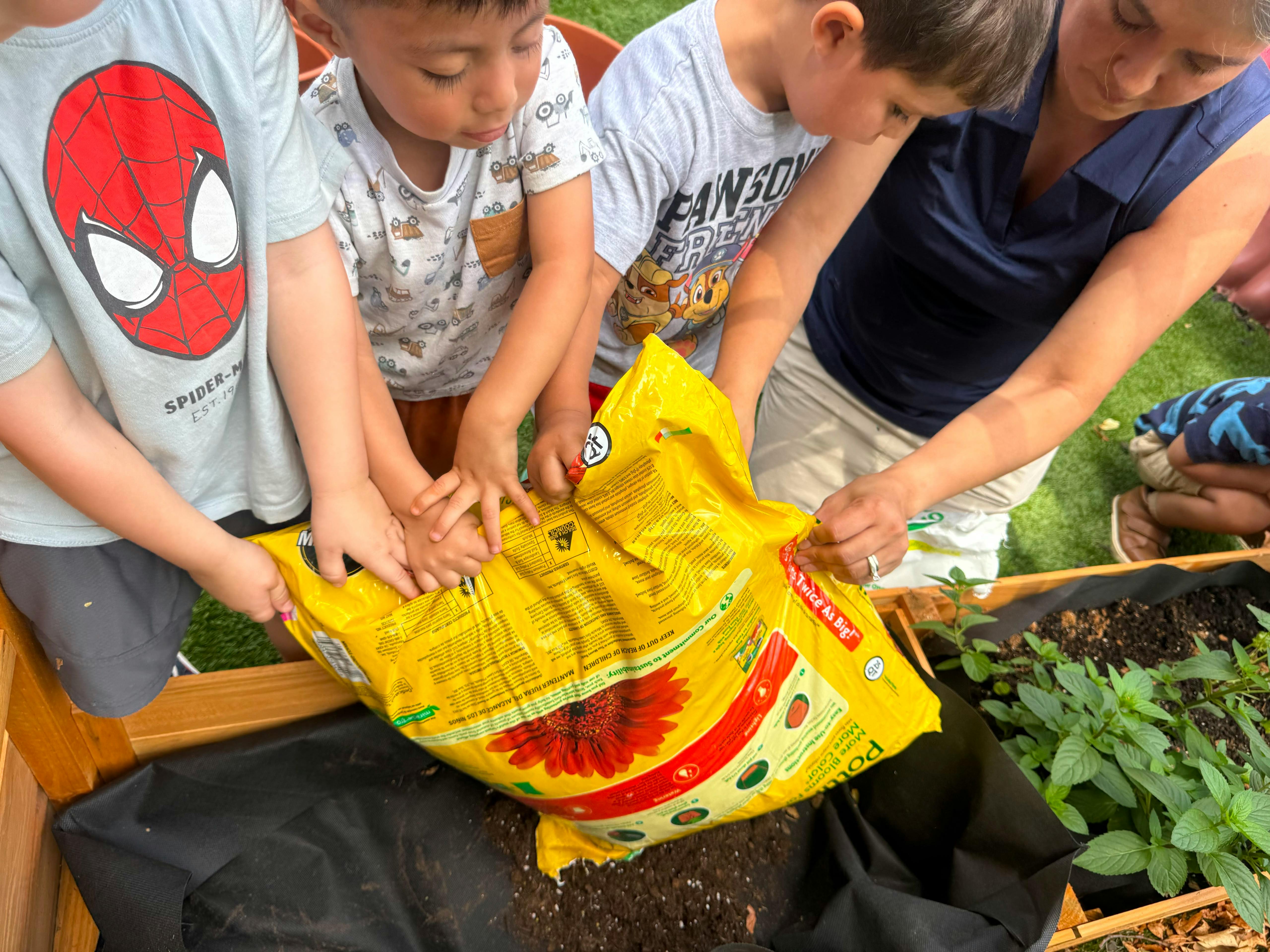 Group of people pouring soil from a bag into a wooden garden bed