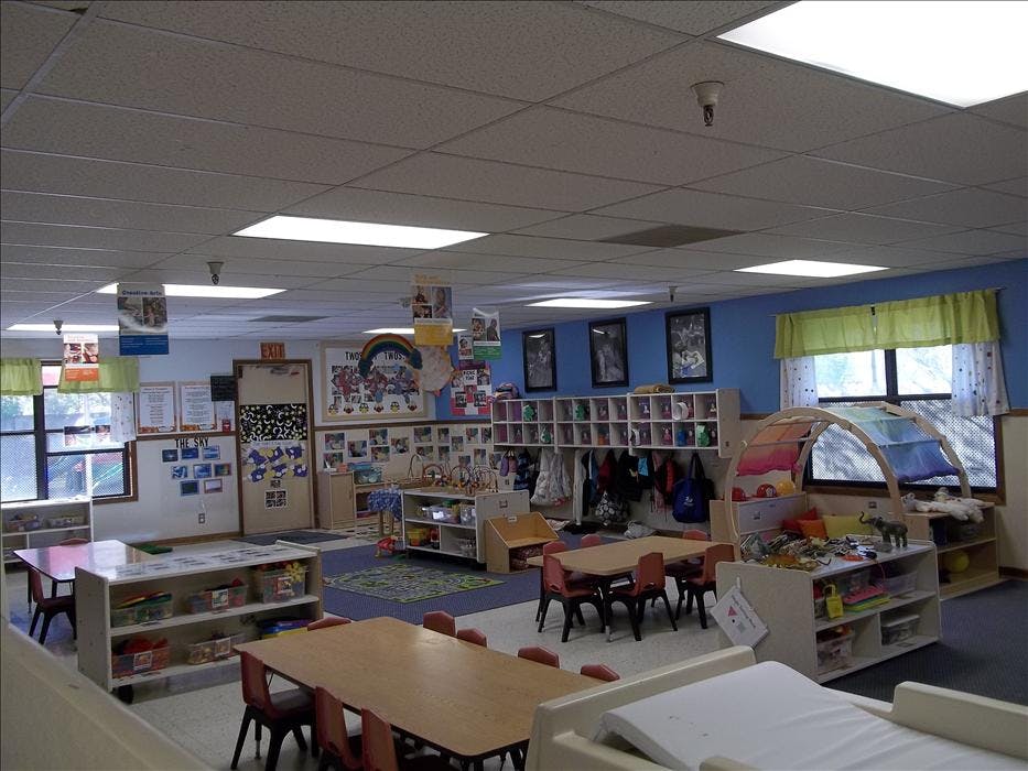 An empty classroom with tables, chairs, shelving units, and windows