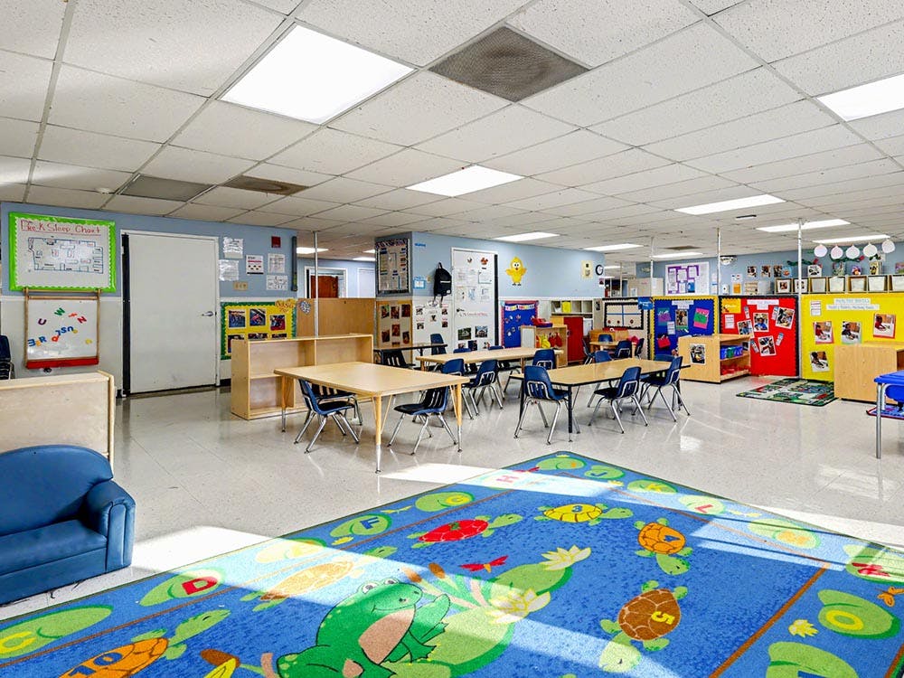 An empty classroom with small tables and chairs, a blue sofa, and a colorful rug