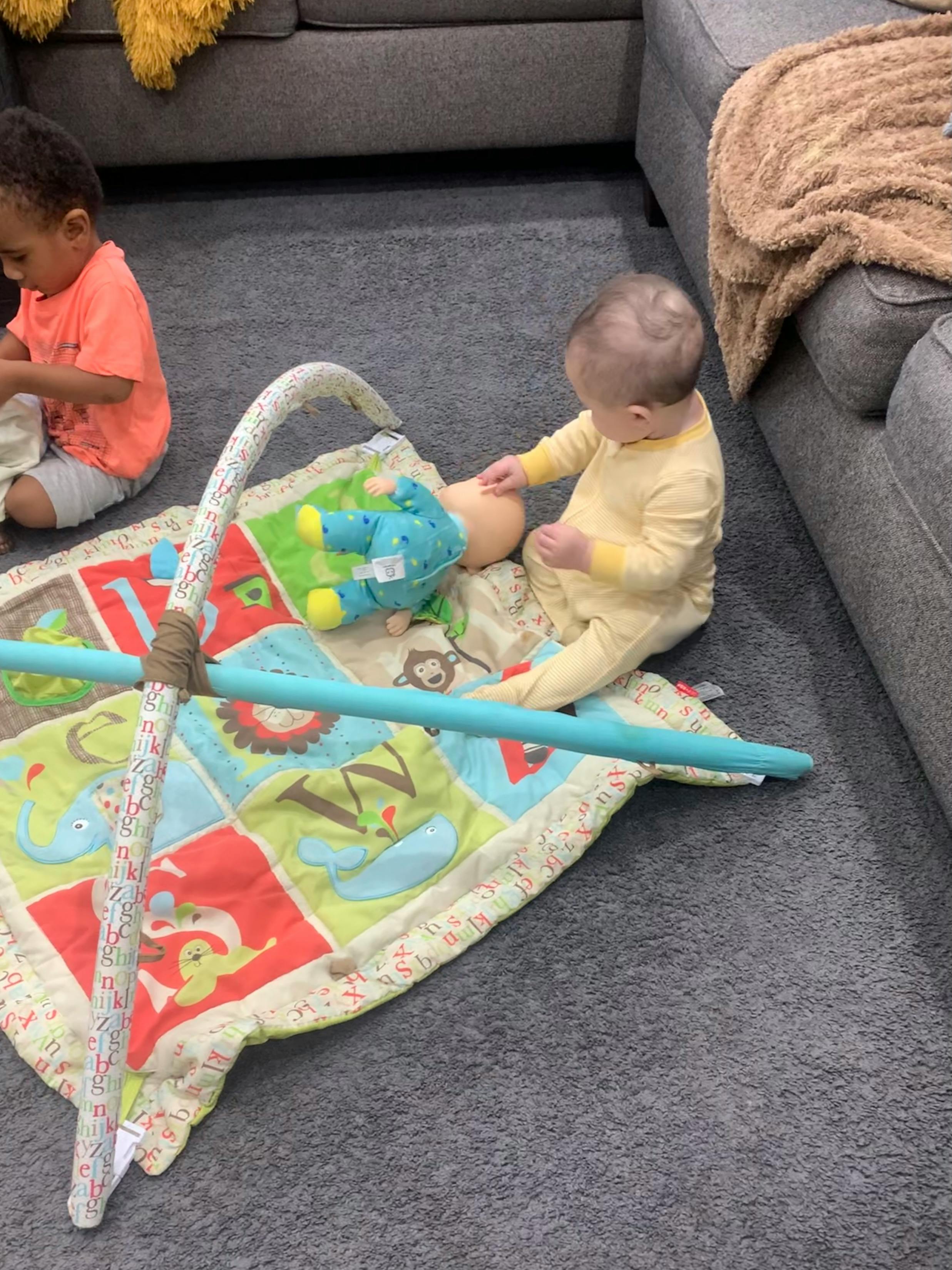 Two children playing on a colorful mat with toys