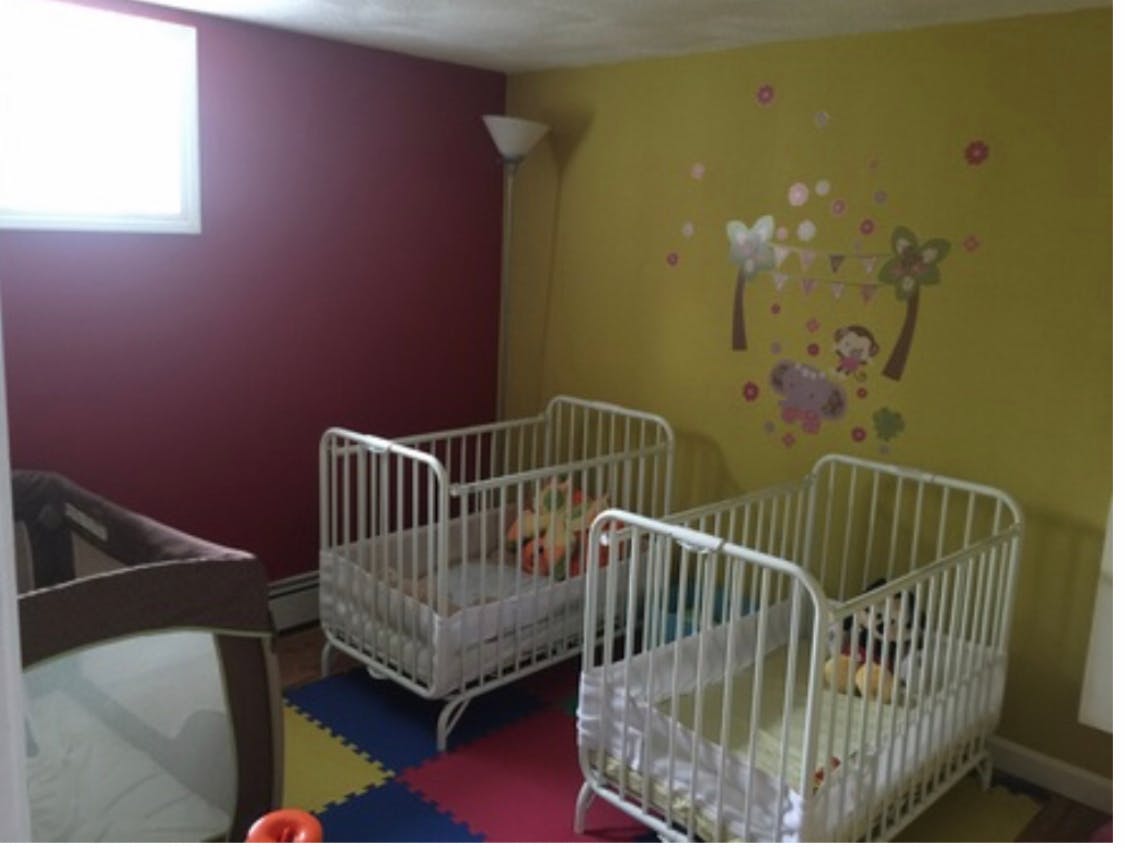 Two white cribs and one brown playpen in a room with colorful floor mats