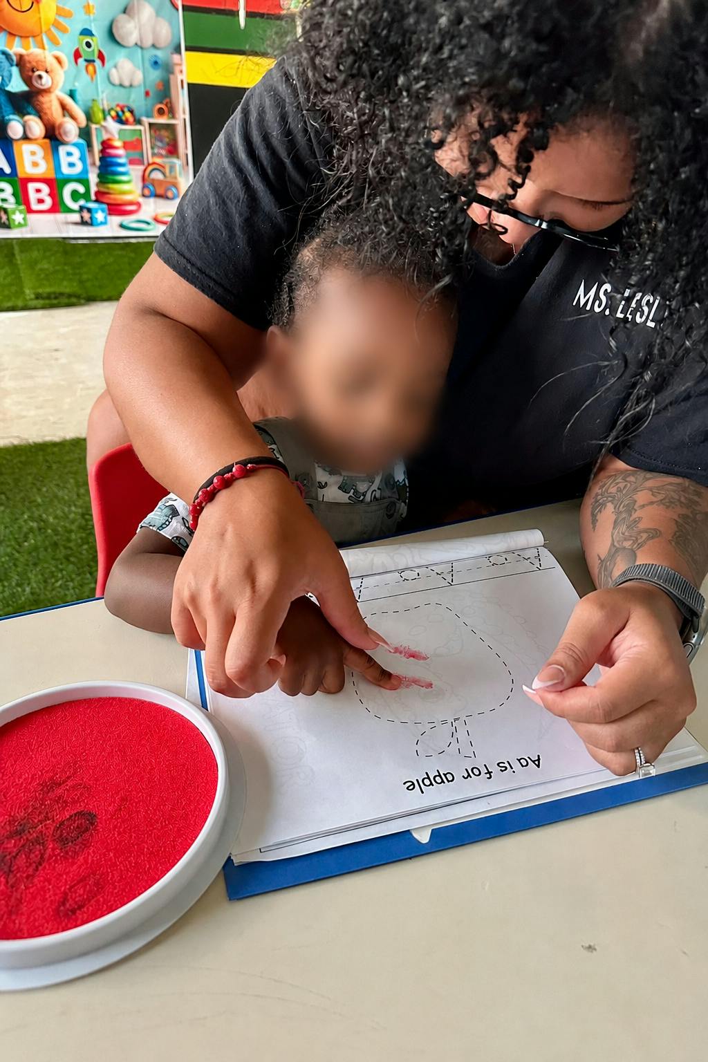 Adult assisting a child with a finger painting activity on a worksheet