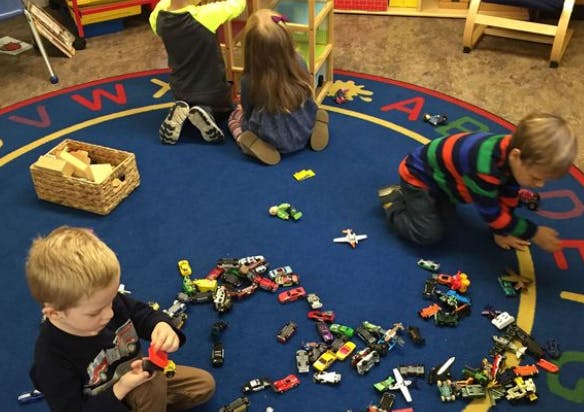 Three children playing with toy cars on a blue rug