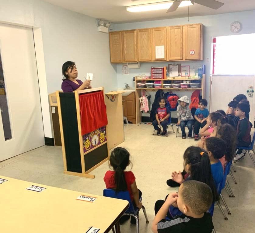 Person at a puppet stage presenting to children in a classroom