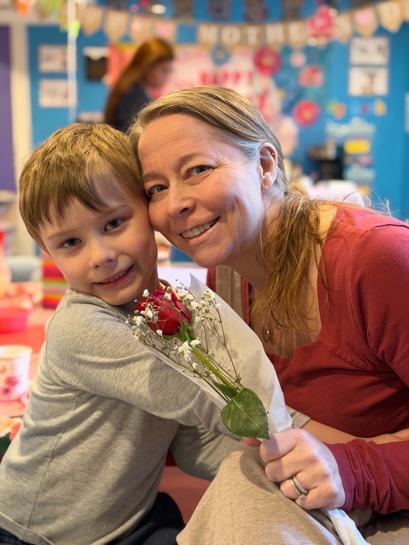 Adult and child embracing with a single red rose