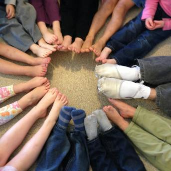 Multiple people sitting in a circle with their feet touching in the center