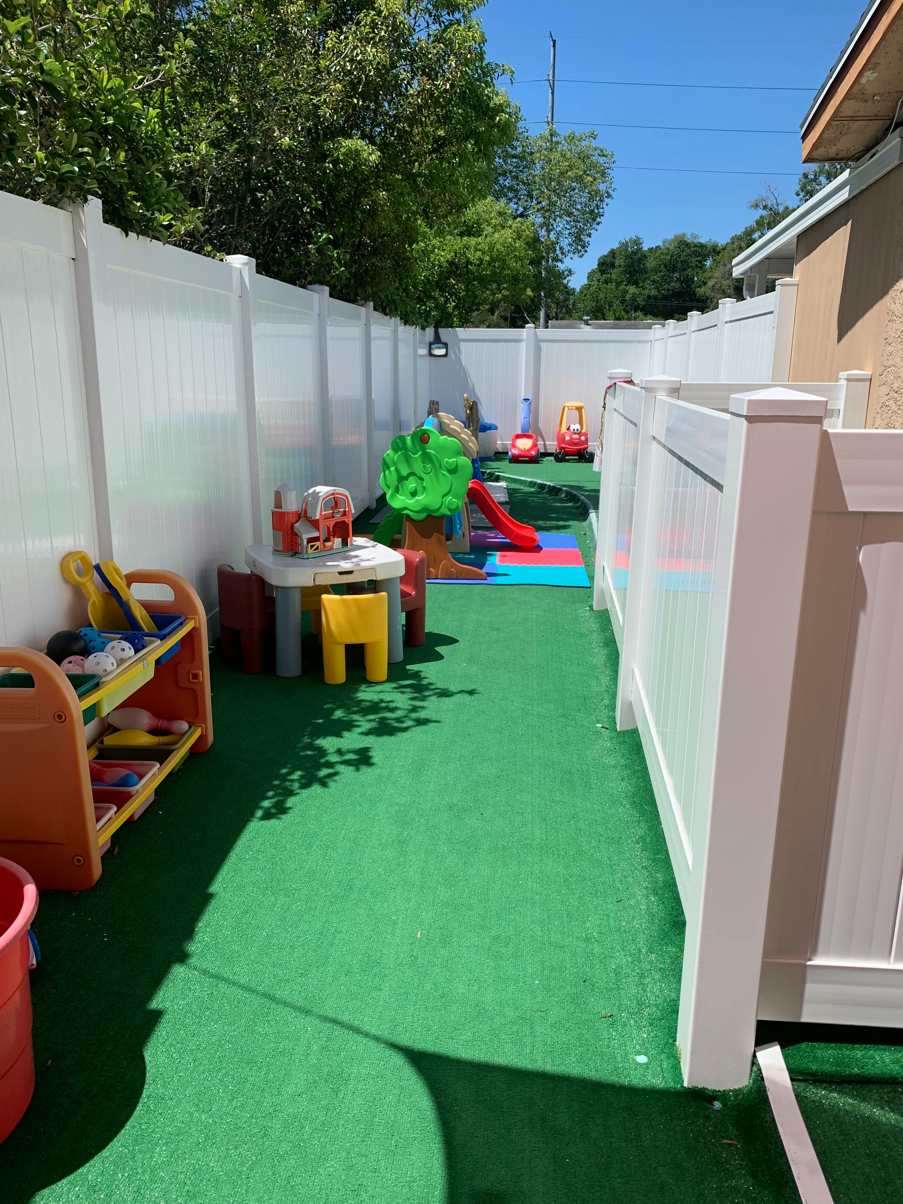 Outdoor play area with artificial turf, white fences, and children's toys