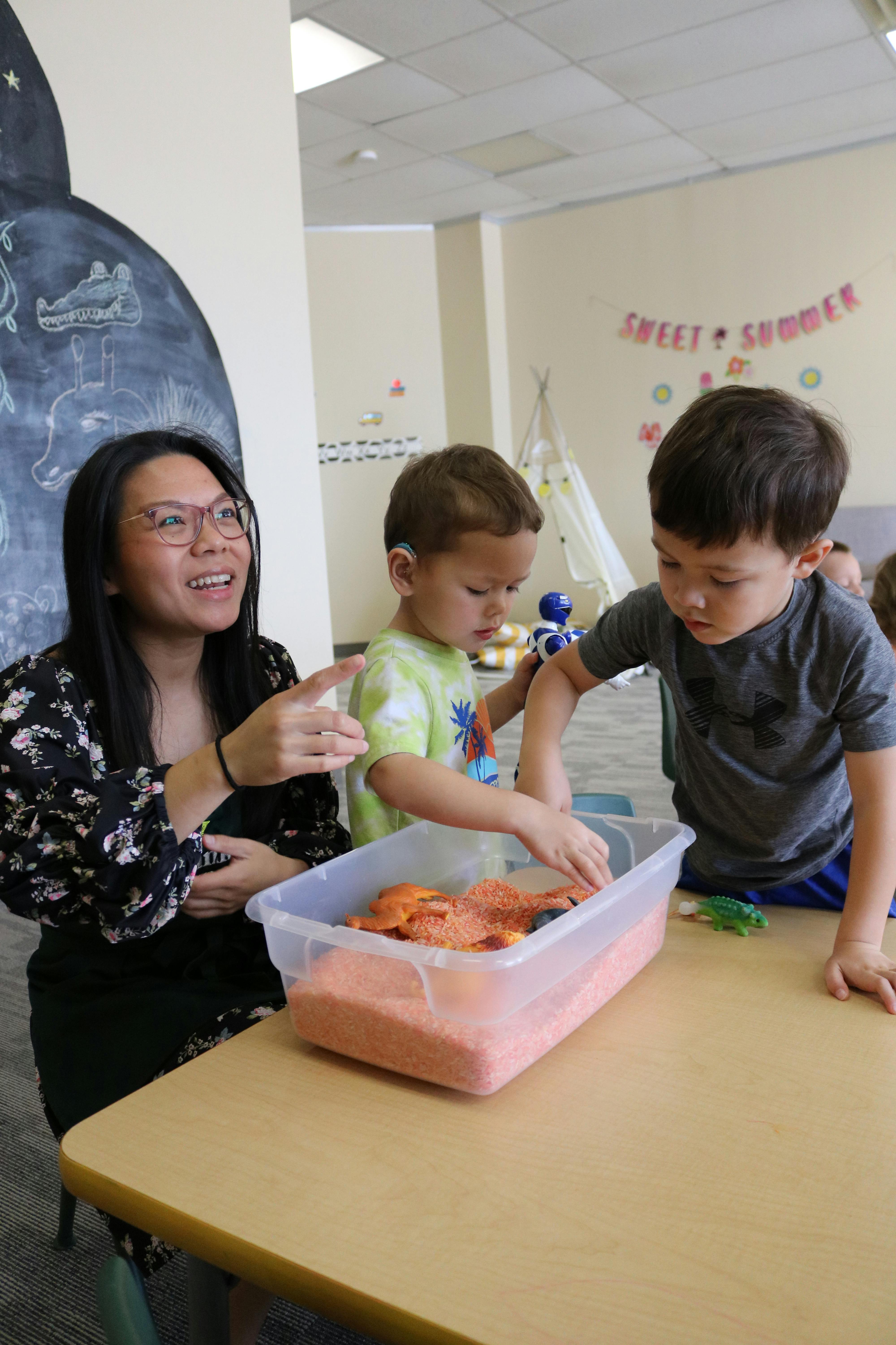 Person and two children playing with sensory bin in a classroom