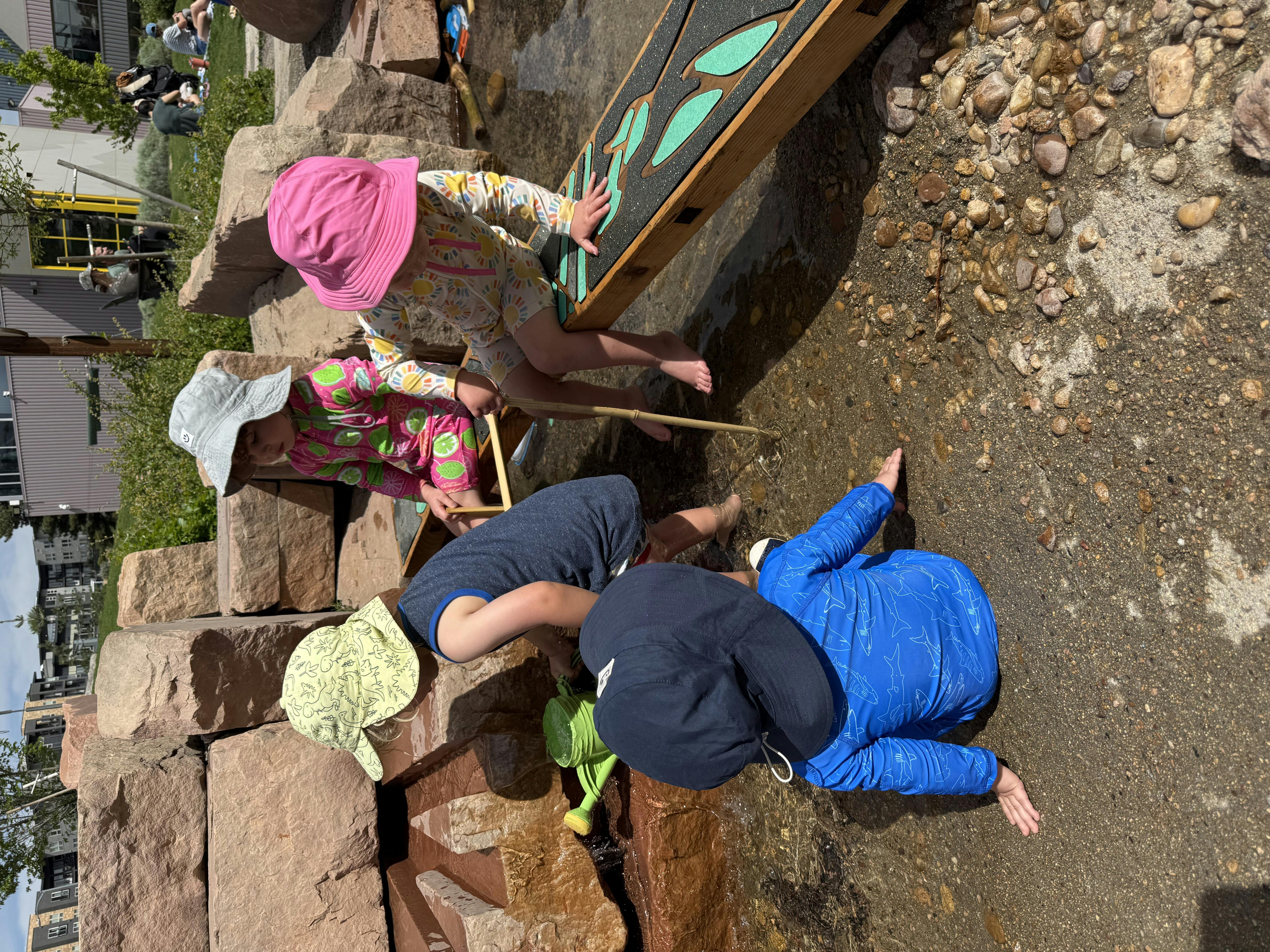 Children playing in a water feature with rocks and a wooden board