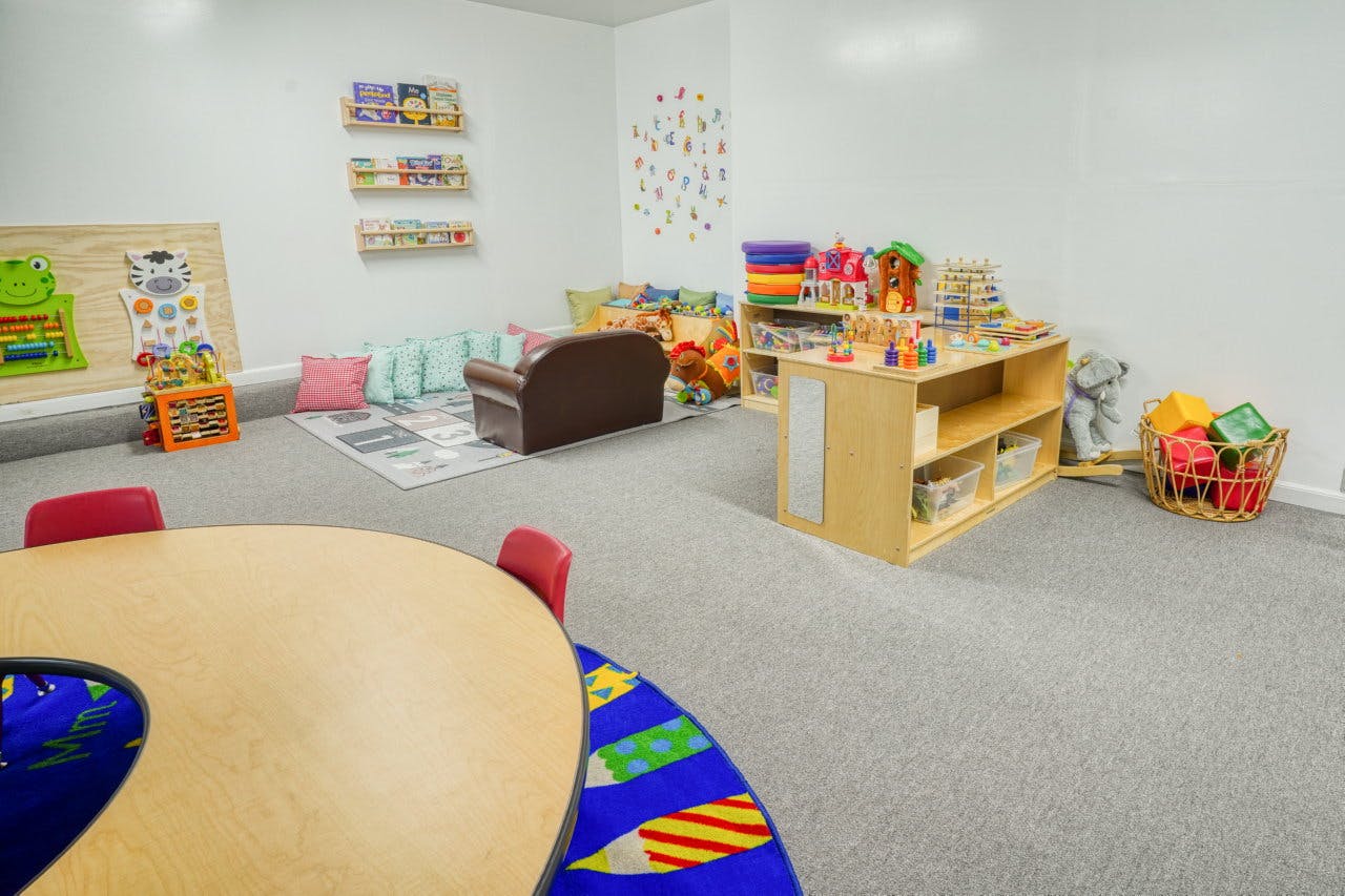 Classroom with a round table, small chairs, and shelves with toys