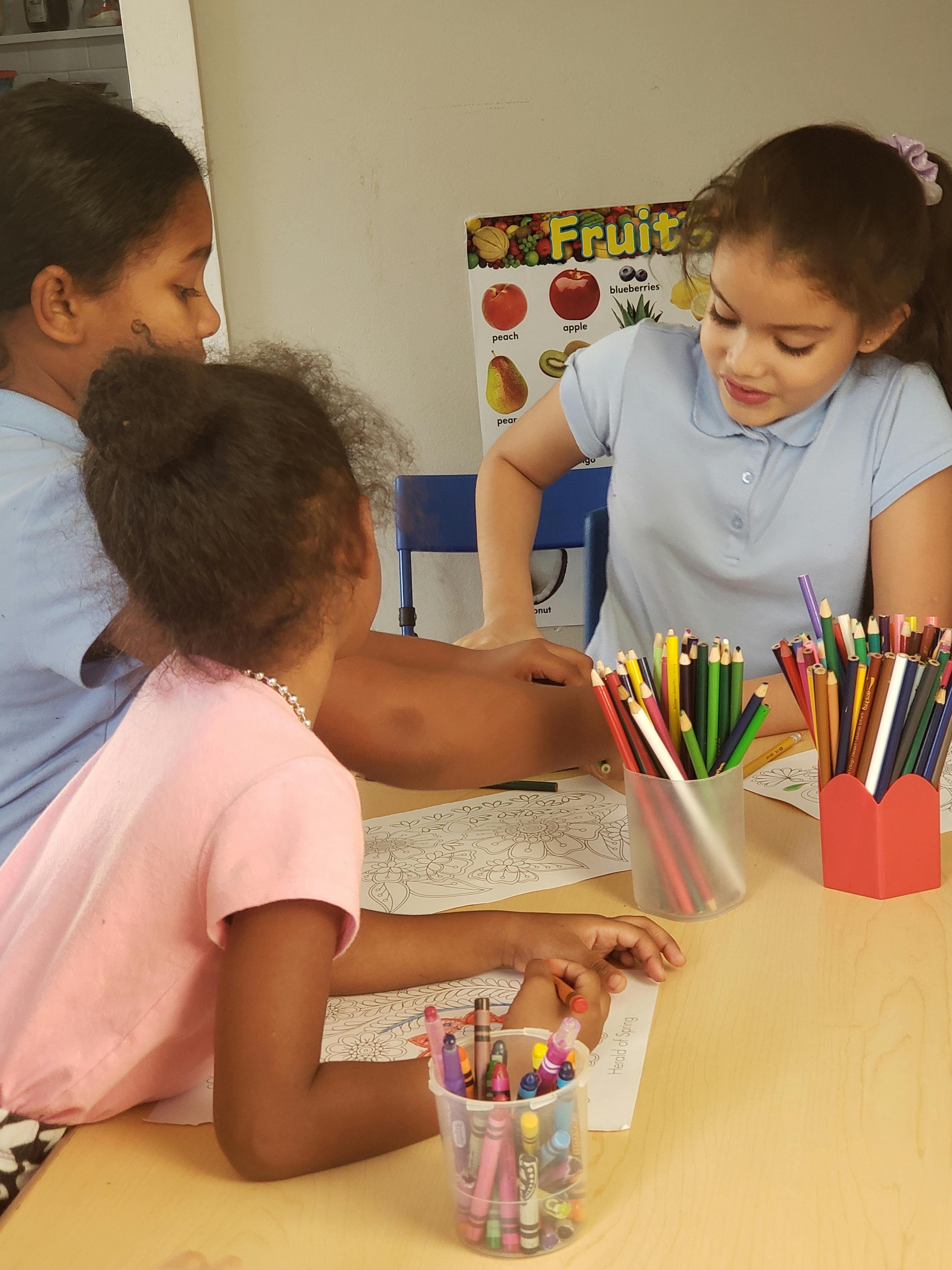 Three children drawing at a table with colored pencils and crayons