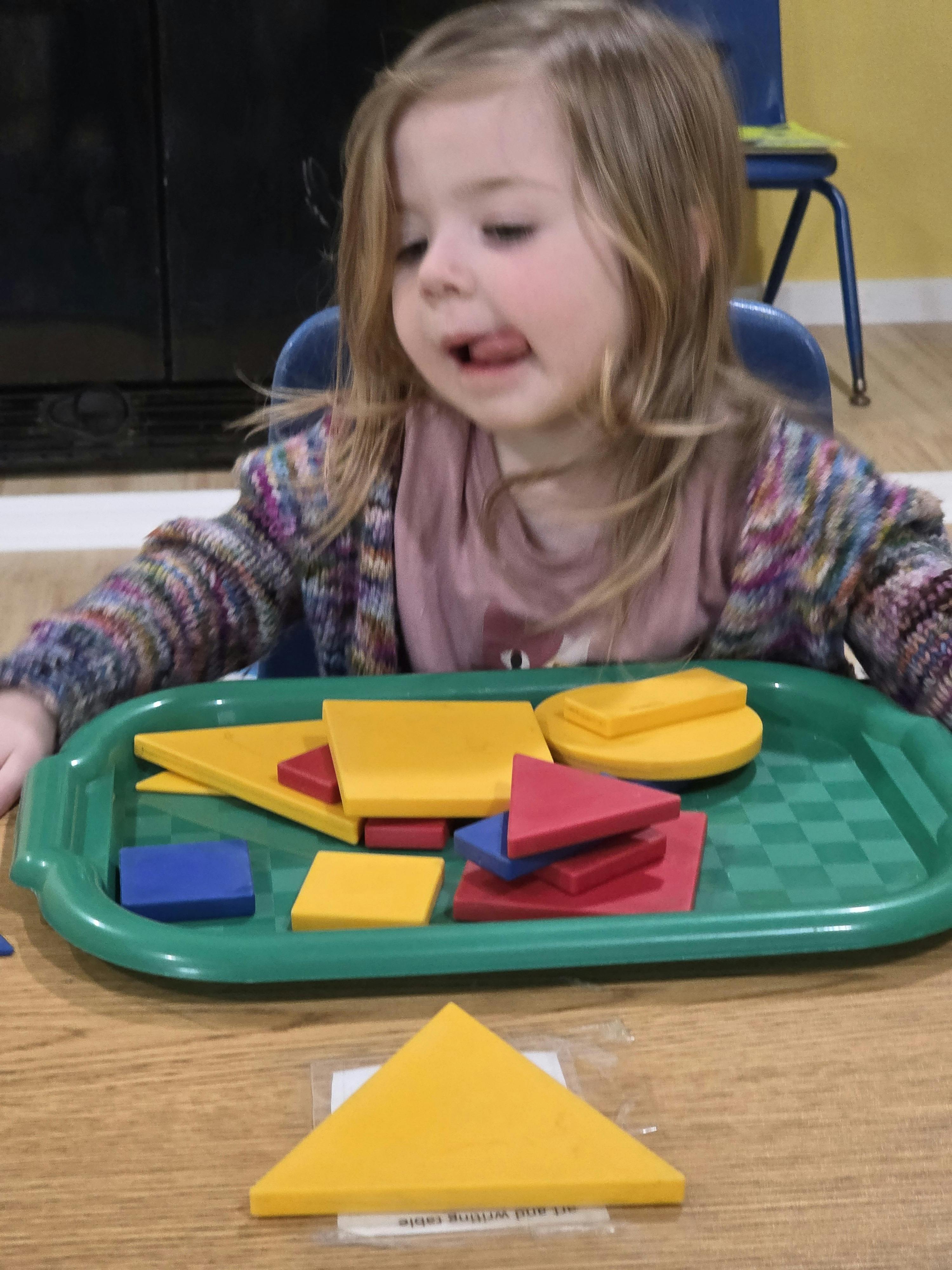 Child playing with colorful geometric pattern blocks on a tray