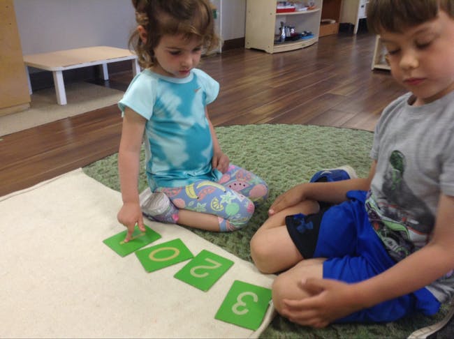 Child pointing at number cards on the floor next to another child